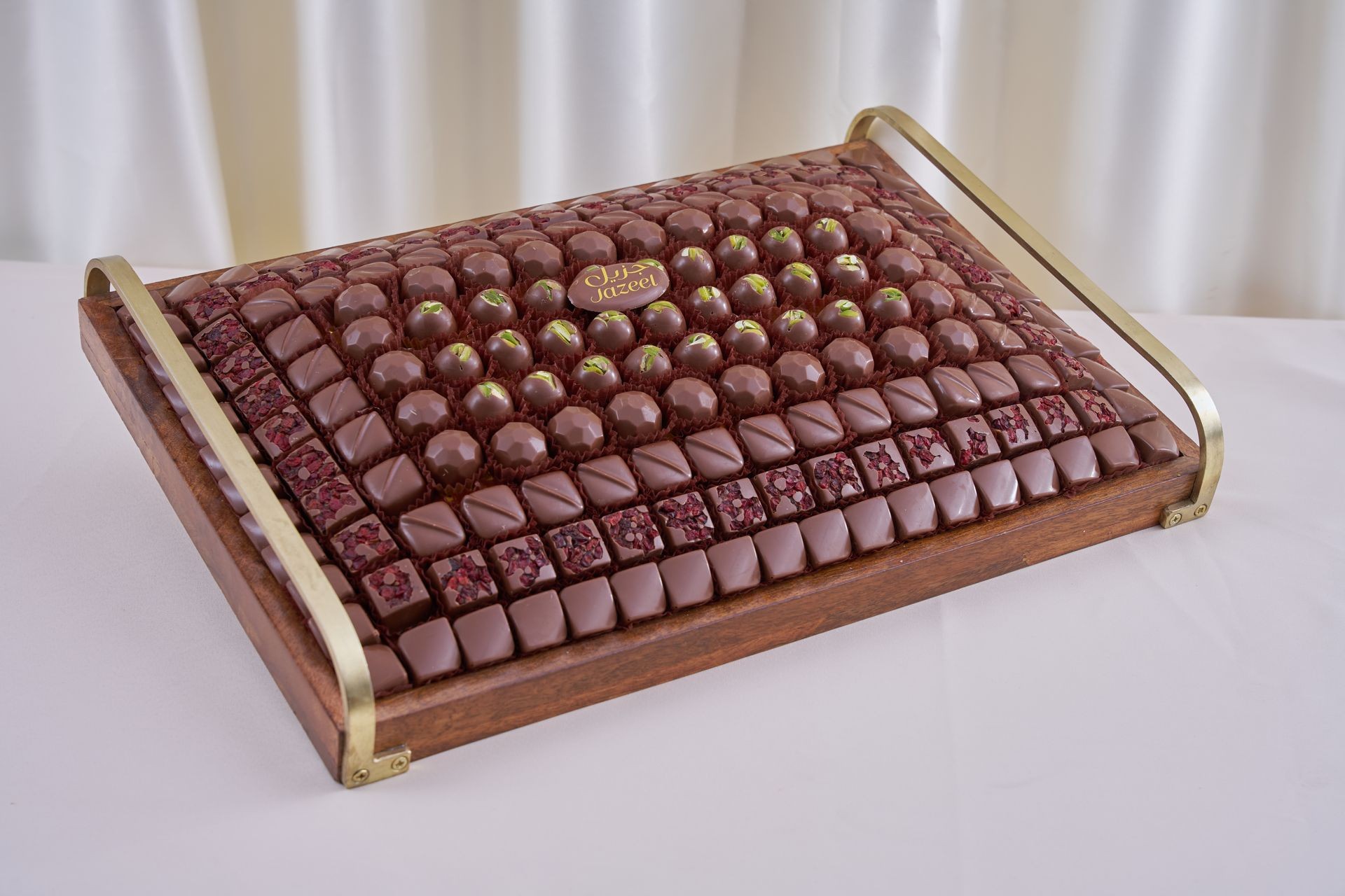 Assorted chocolates arranged on a decorative wooden tray with brass handles.