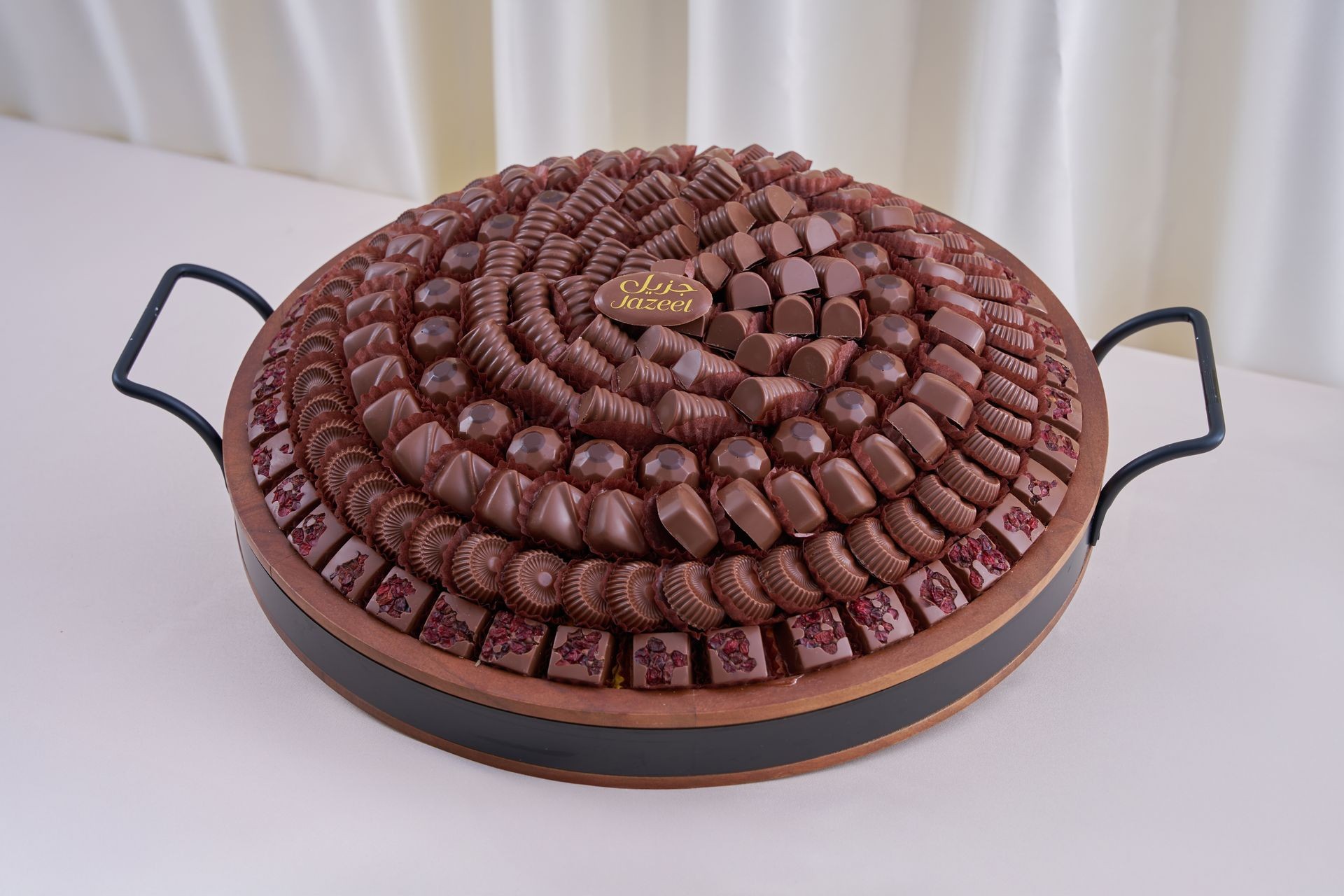 Large round tray filled with assorted chocolates arranged in circular patterns.