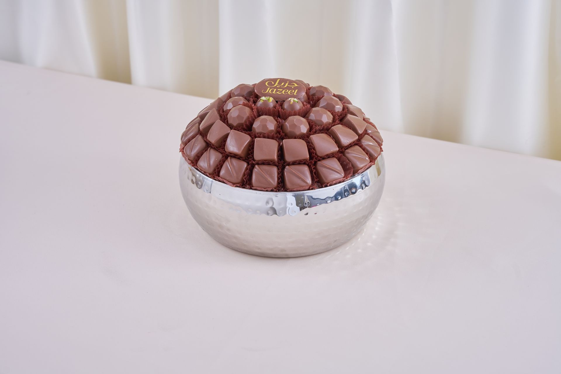 Silver bowl filled with neatly arranged chocolate pieces on a white surface.