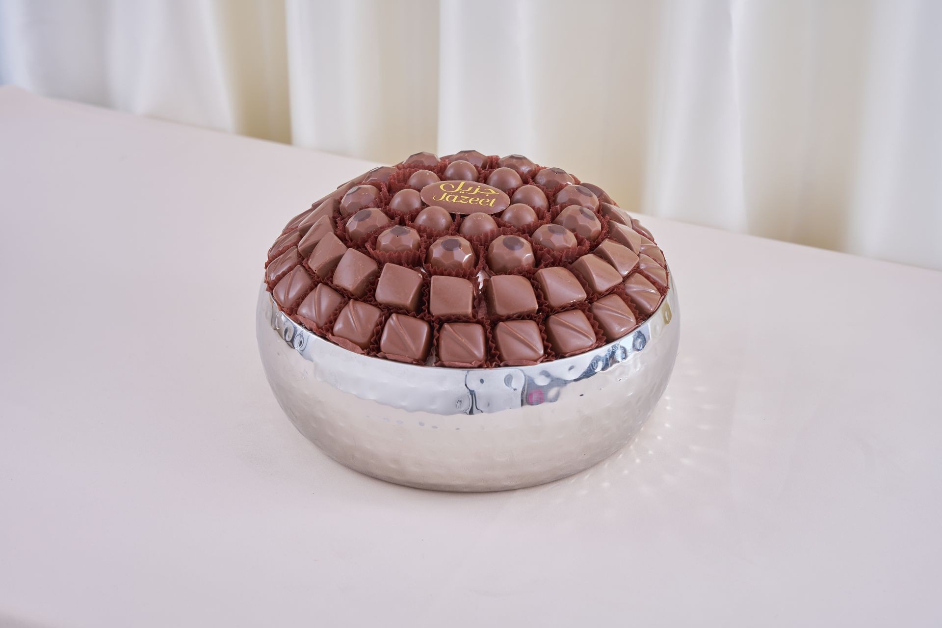 Assorted chocolates arranged neatly in a round silver bowl on a white table.