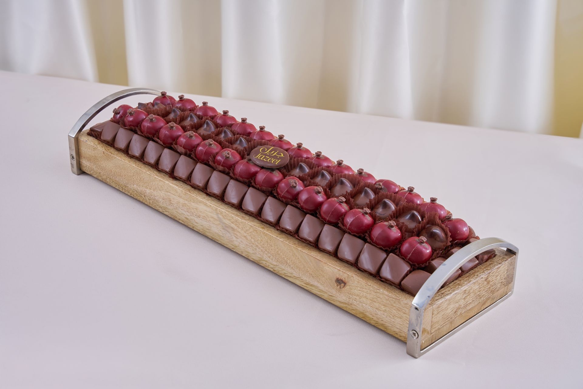 Assortment of red and brown chocolates arranged on a wooden tray with metal handles.