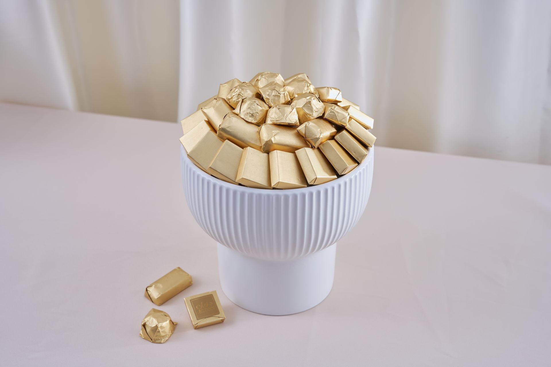 White bowl filled with gold-wrapped chocolates on a light surface.