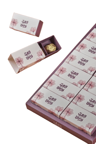 Elegant box containing individually wrapped chocolates, with pink flower design and Arabic script on the packaging.