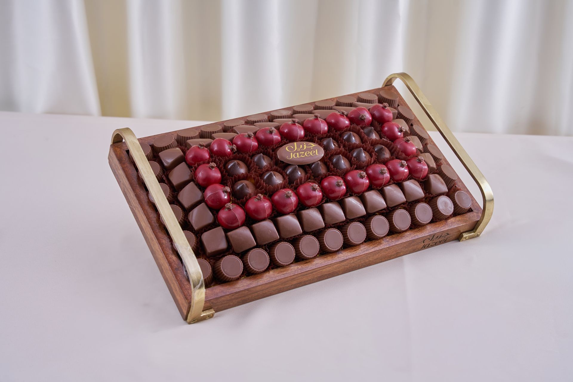 Elegant display of assorted chocolates and red fruit on a wooden tray with golden handles.
