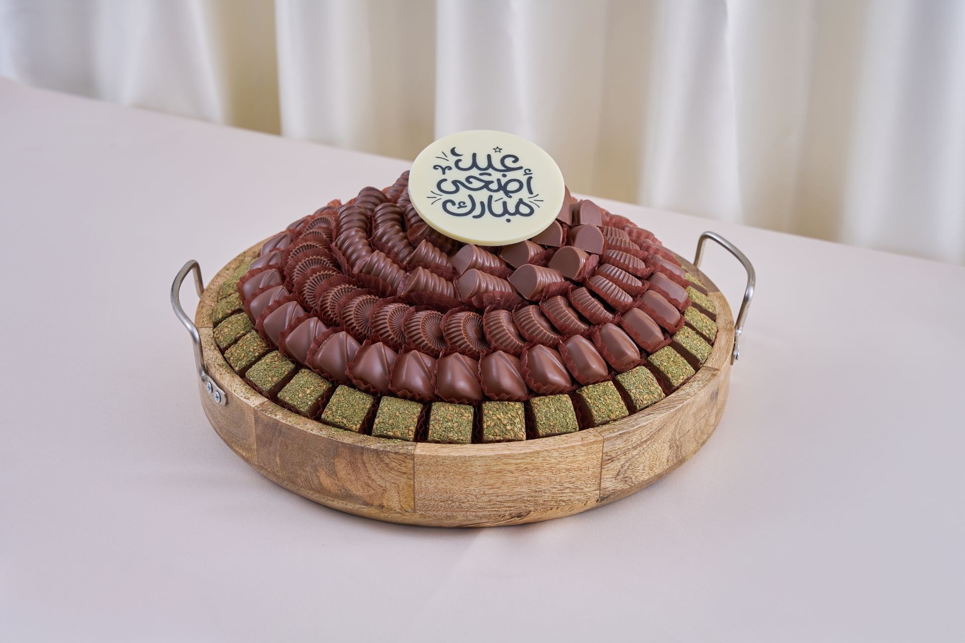 Chocolate arrangement in a wooden tray with a circular plaque on top featuring Arabic calligraphy.