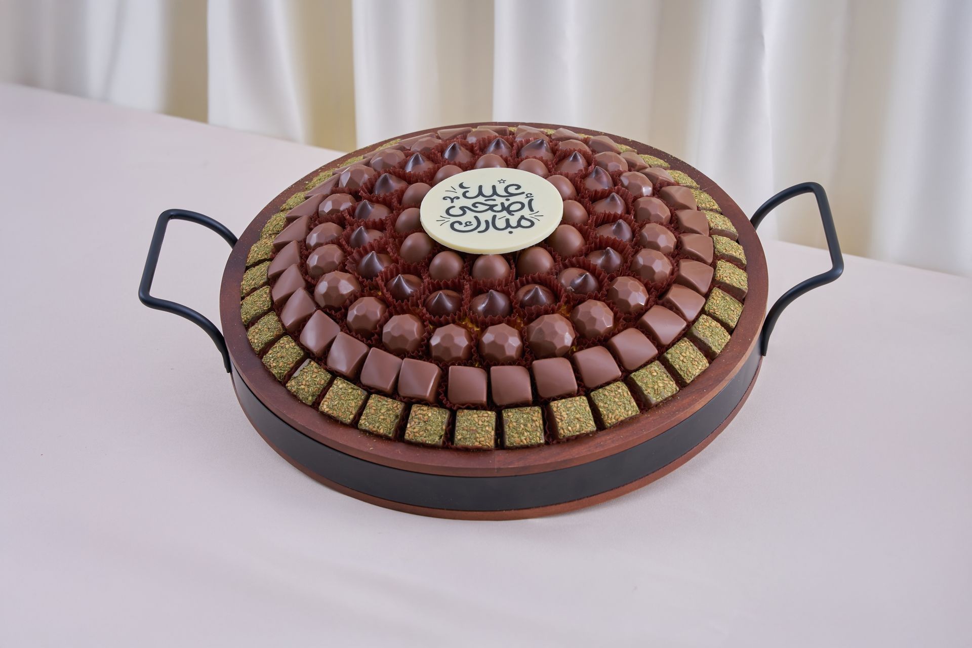 Assorted chocolates and sweets arranged in a circular tray with Arabic writing on a central piece.