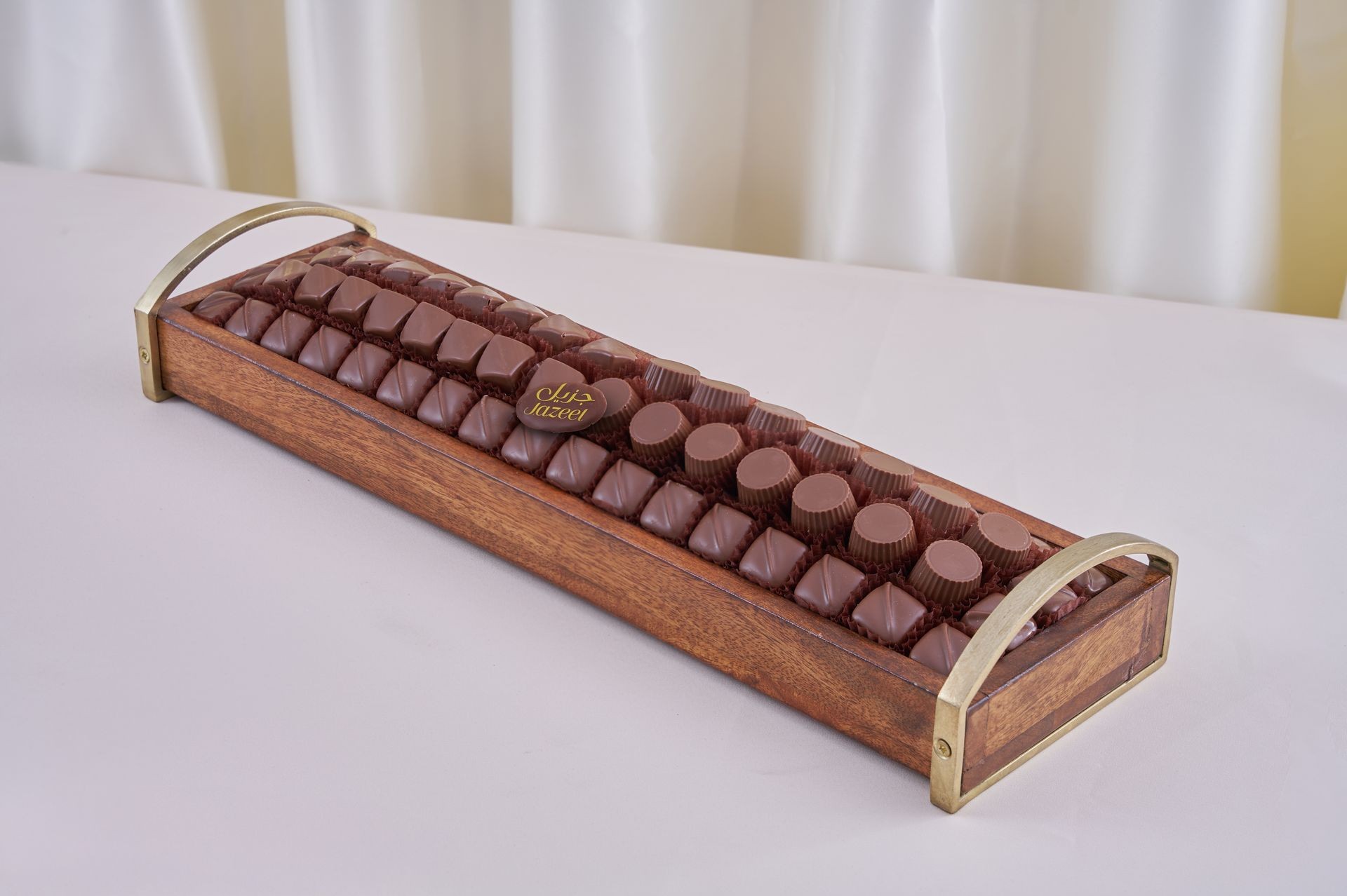 Wooden tray filled with assorted chocolate pieces on a white tablecloth.