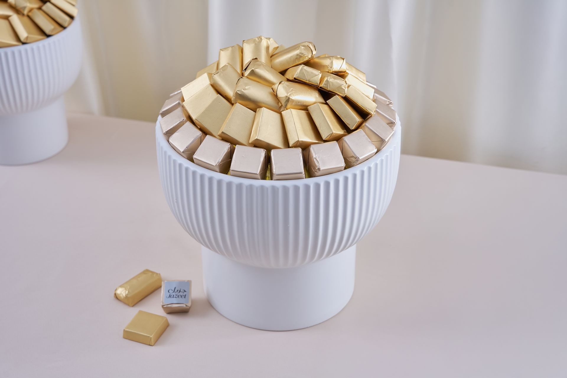 White bowl filled with gold and silver-wrapped chocolates on a table.