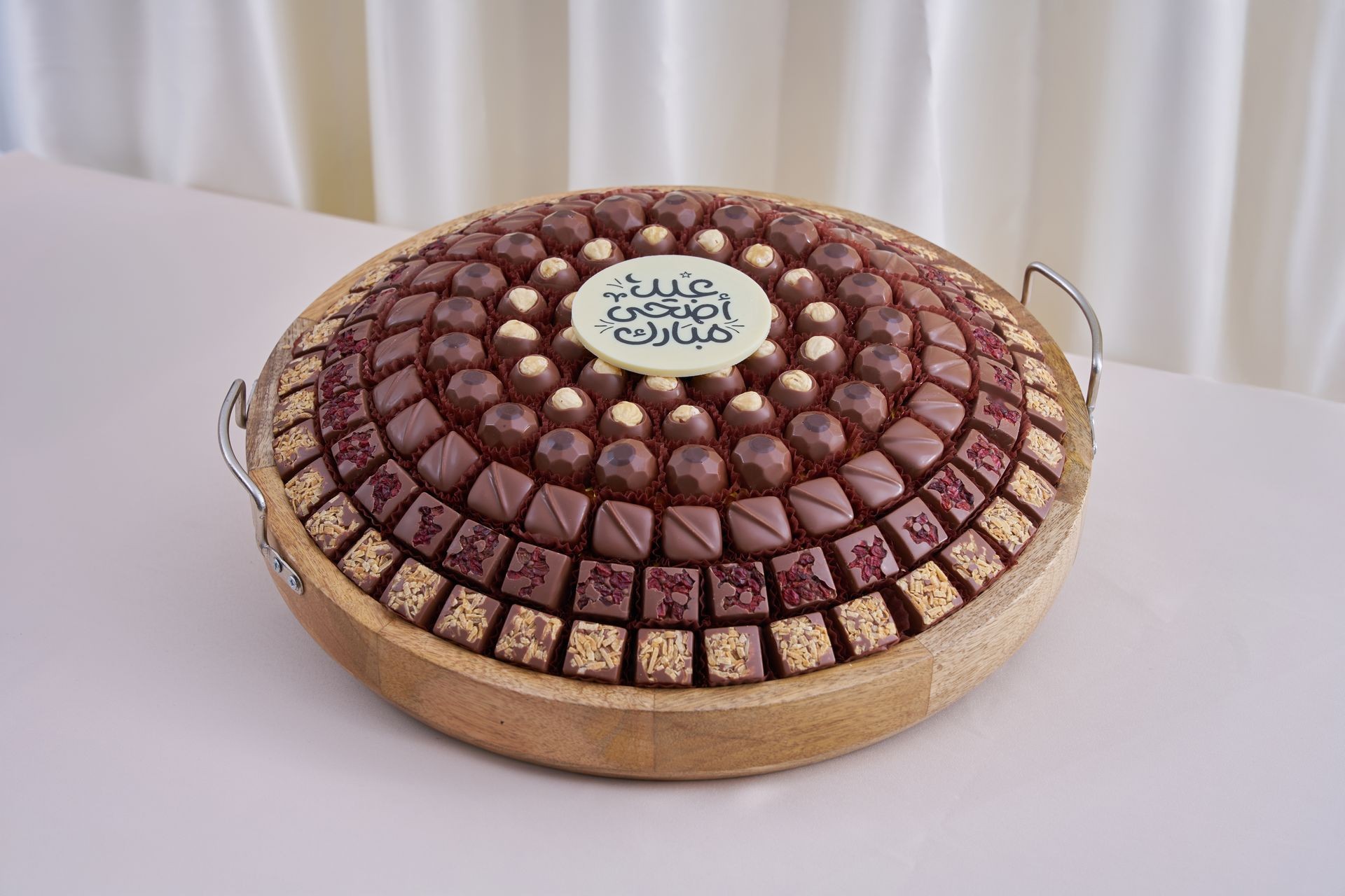 Assortment of chocolates arranged in circles on a wooden tray with decorative text on top.
