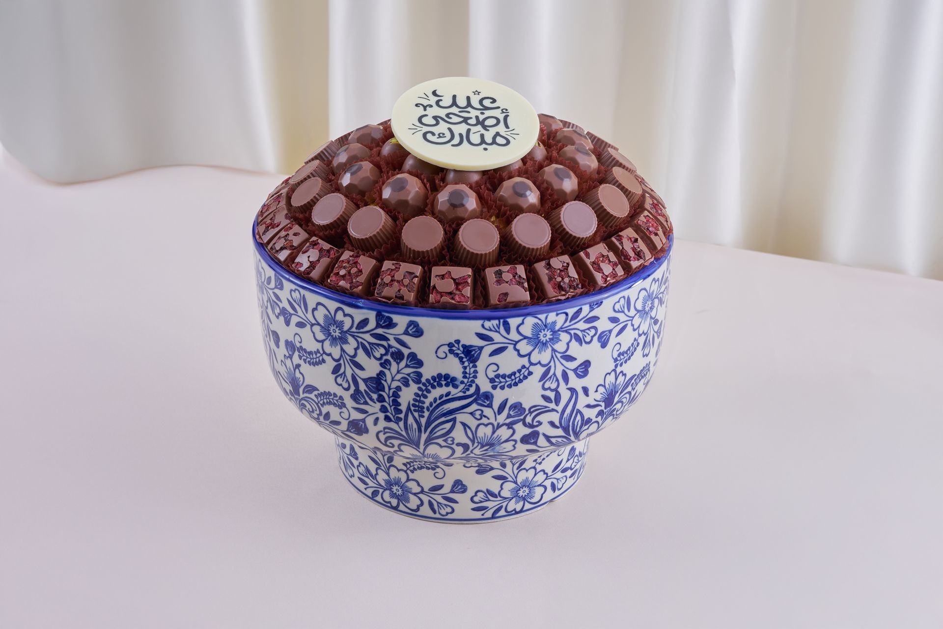 Elegant floral blue and white ceramic bowl filled with assorted chocolates topped with a decorative white disc.